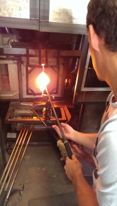 man putting rod with molten glass in furnace for reheating
