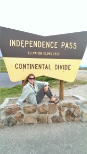 woman sitting under continental divide sign with mountains in background