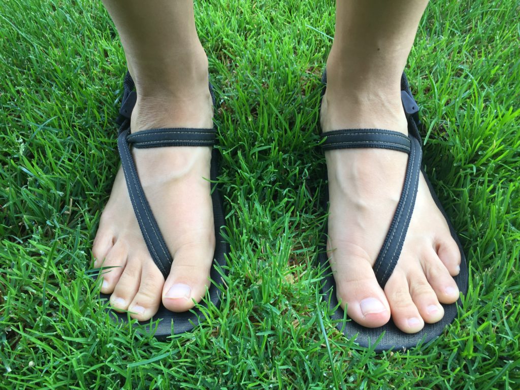 earth runners sandals with different ankle strap twists on green grass background